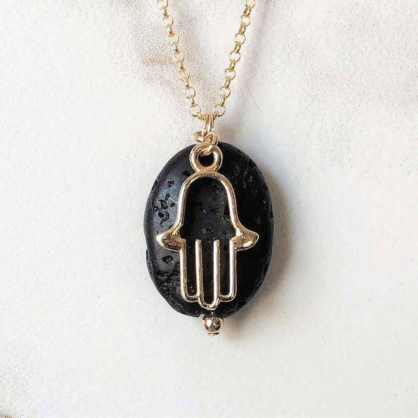 A close up of the gold hamsa charm and black lava bead on the aromatherapy necklace