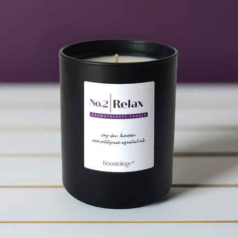 A black aromatherapy candle jar on a white wooden shelf with a purple wall