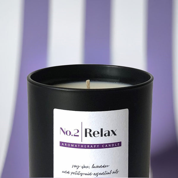 A black scented candle jar with purple and white striped wallpaper