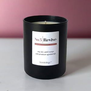 A black aromatherapy candle on a grey shelf with a pink wall