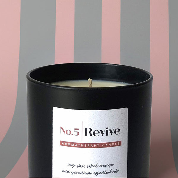 A black scented candle with grey and pink wallpaper