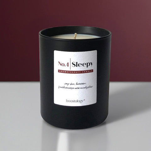 A black aromatherapy candle on a grey shelf with a dark red wall behind