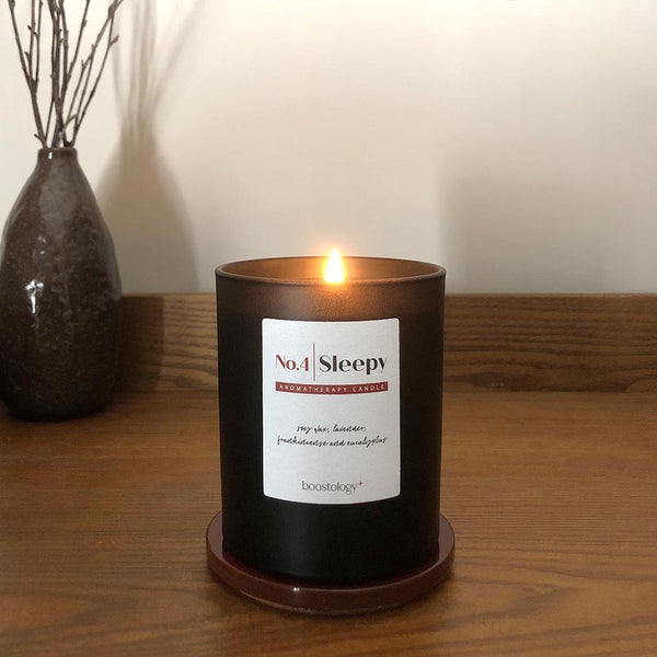 A lit soy wax candle on a wooden bedside table