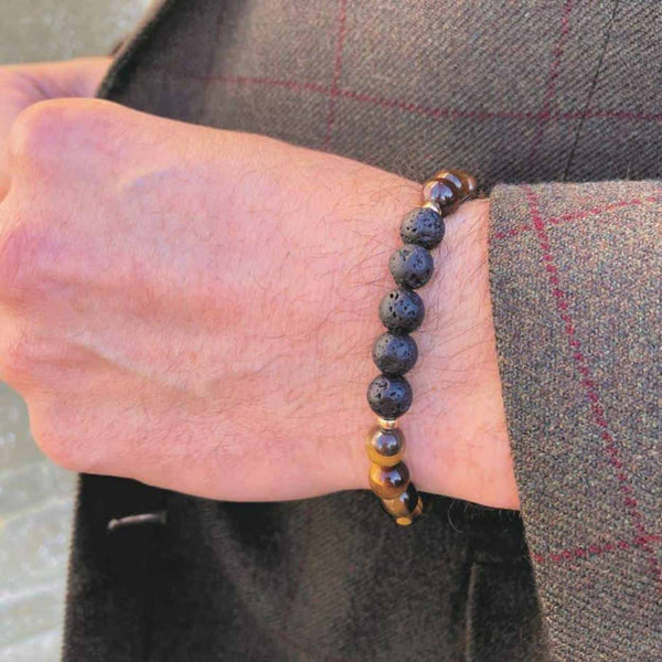 A man wearing a brown jacket with a tigers eye aromatherapy bracelet